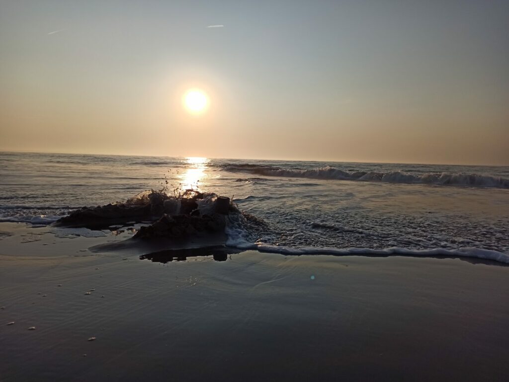 Eine Welle bricht sich an einer Sandburg bei Sonnenuntergang